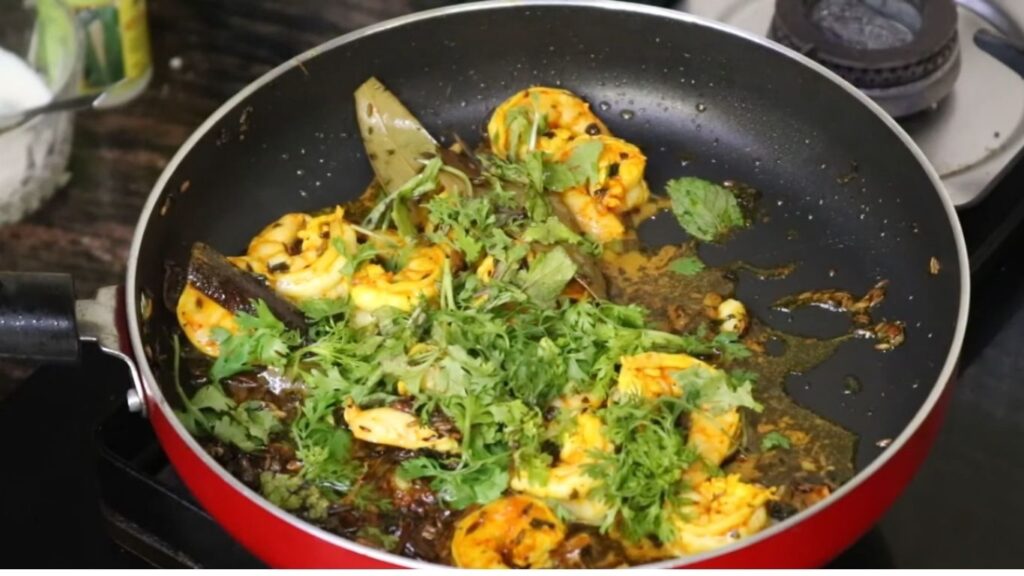 Succulent prawns turning pink in a pan, sautéed with finely chopped onions, minced garlic, grated ginger, and diced tomatoes, seasoned with turmeric and garam masala, bubbling gently over medium heat