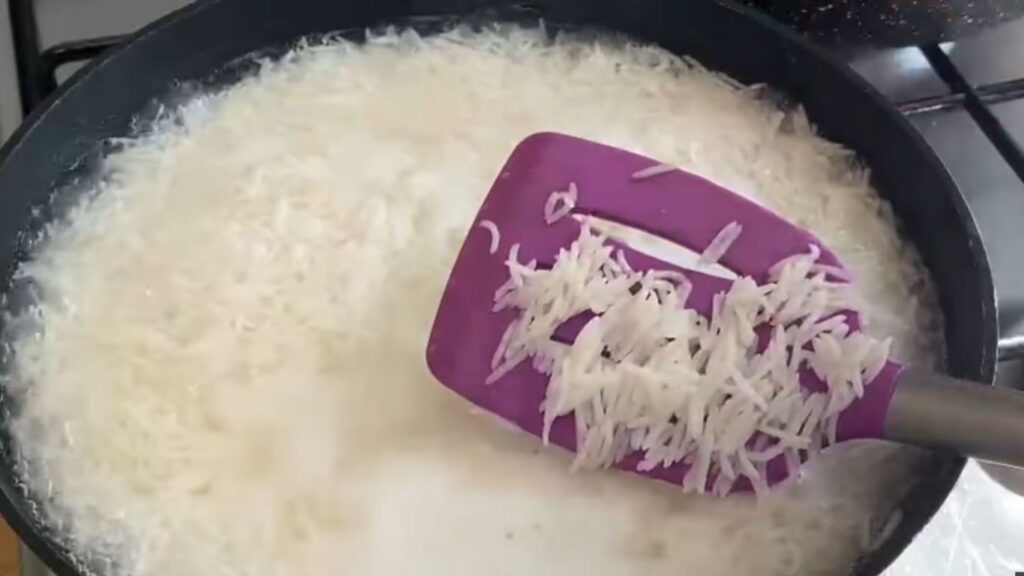 Gluten-Free Chicken Biryani | A Simple Twist on a Classic 3 Partially cook basmati rice in a pot of boiling water. The rice grains are long and white, surrounded by starchy, cloudy water, indicating they are being parboiled.